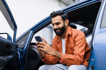 Eastern Man Using Phone Sitting In Auto With Opened Door - obrazy, fototapety, plakaty