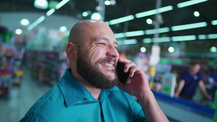 Happy casual Man speaking on phone inside store shed. South American bold person with beard conversing and listening with modern smartphone in ear