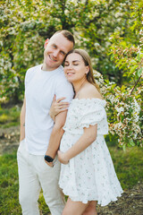 Fototapeta premium Beautiful young couple in spring garden. Beauty lifestyle family concept. A happy mother is expecting a baby. A happy young couple in a blooming garden