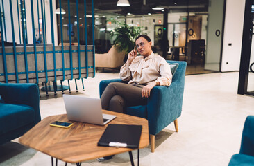 Fototapeta premium Positive female executive in glasses resting on armchair after work on laptop