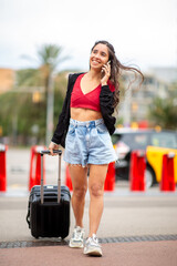 Full length smiling travel girl with suitcase talking on phone