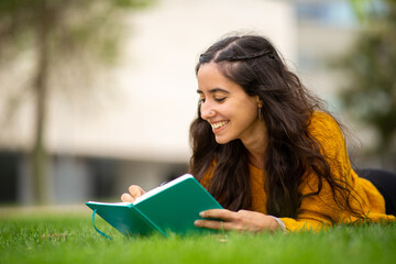 Young woman lying on grass and writing in book
