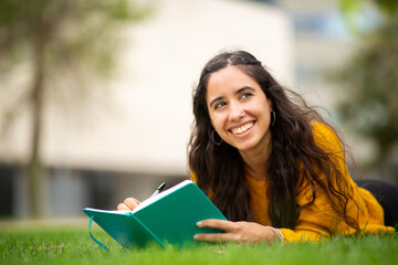Fototapeta premium smiling young woman lying on grass with book and pen