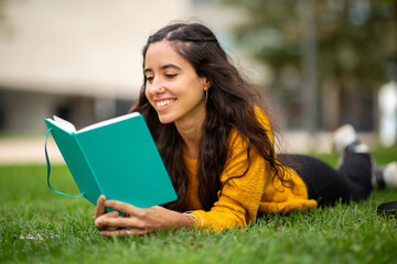 Fototapeta premium smiling young woman lying on grass and reading book