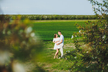 Fototapeta premium The concept of happy family relationships. A young happy couple in anticipation of pregnancy walks through a blooming garden. Couple in love in blossoming apple trees.