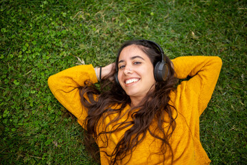 smiling young woman lying on grass and listening to music with headphones