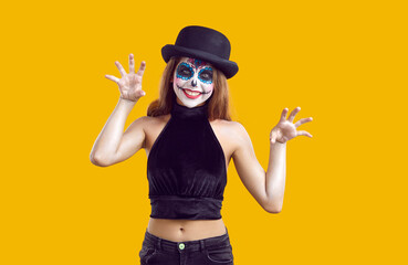 Happy girl in black costume and witch hat with creative skull makeup is having fun at Halloween...