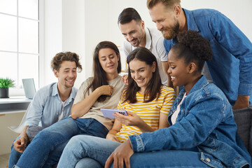 Young people watching something on a modern mobile phone. Group of happy diverse friends sitting on the sofa at home, looking at a smartphone, watching a funny video and smiling