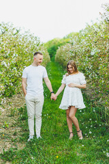 Naklejka na ściany i meble Beautiful young couple in spring garden. Beauty lifestyle family concept. A happy mother is expecting a baby. A happy young couple in a blooming garden