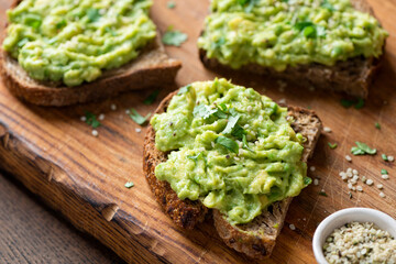 Toast with mashed avocado, seeds and parsley on a wooden plate, closeup view. Healthy vegan snack...