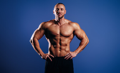 Fototapeta na wymiar Handsome muscular man athlete posing on blue background. Strong bodybuilder with prefect body