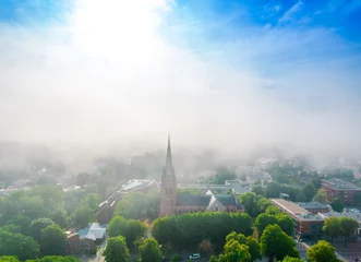 Fotobehang Church of Saint Marie in haze in Palanga, Lithuania. Aerial view on a foggy day. Low clouds over the city © Audrius