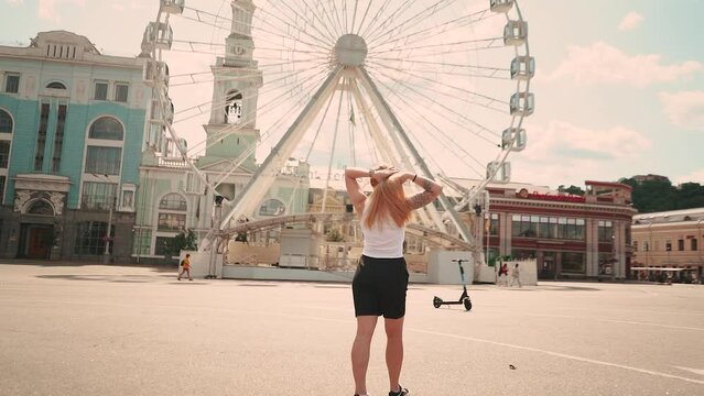 a beautiful girl in a white T-shirt poses in Kyiv against the backdrop of a Ferris wheel in the city center in summer