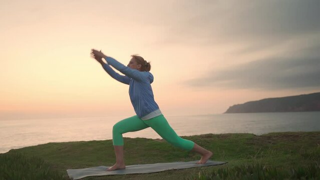 Senior woman practicing yoga asanas ocean background. Mature female doing yoga exercise on beach during sunset. Retirement, relaxation, vacation, healthy senior lifestyle