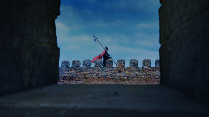 Roman guard patrols with a spear on a citadel wall at night. View from behind a wall battlement