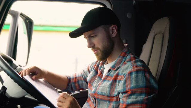Delivery man with cardboard box checking list in truck. Courier checking list on clipboard. Deliveryman sitting in truck and checking the delivery list. Right hand drive car