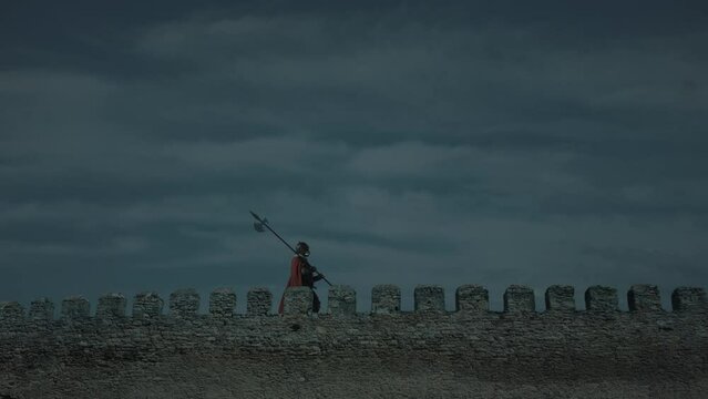 Roman soldier with spear on a fortress wall with defensive battlements. Slow motion