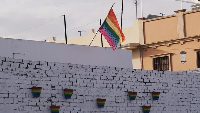 On the roof of the house, an LGBT flag flutters in the wind, flower pots painted in rainbow colors are hung on a white fence.