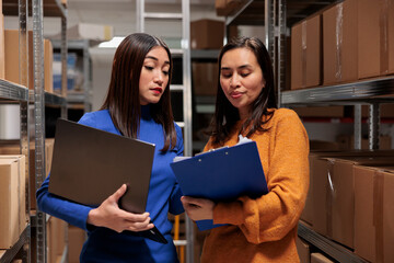 Warehouse asian women employees managing products stocking and distribution. Storehouse managers checking goods in storage, doing inventory using data on clipboard and laptop