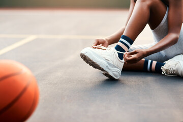 I dont want to trip of the court. Cropped shot of an unrecognizable sportswoman sitting on the court and tying her shoelaces before playing a game of basketball.