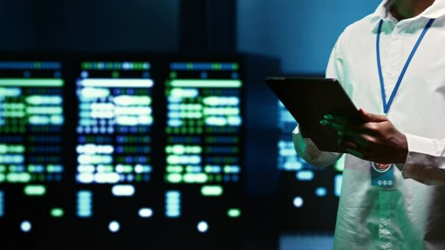 IT specialist walking through server rows performing data backups, close up. Serviceman using tablet to make sure electric generators are able to ensure operational continuity