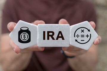 Man holding foam plastic blocks with icons and sees abbreviation: IRA. Concept of IRA Individual Retirement Account. Choice of traditional IRA or roth IRA retirement plans.