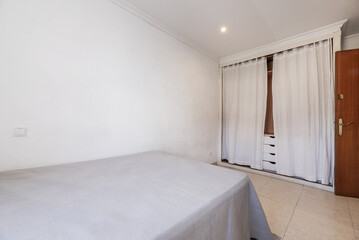 Bedroom with a double bed with a gray bedspread, a built-in wardrobe with curtains