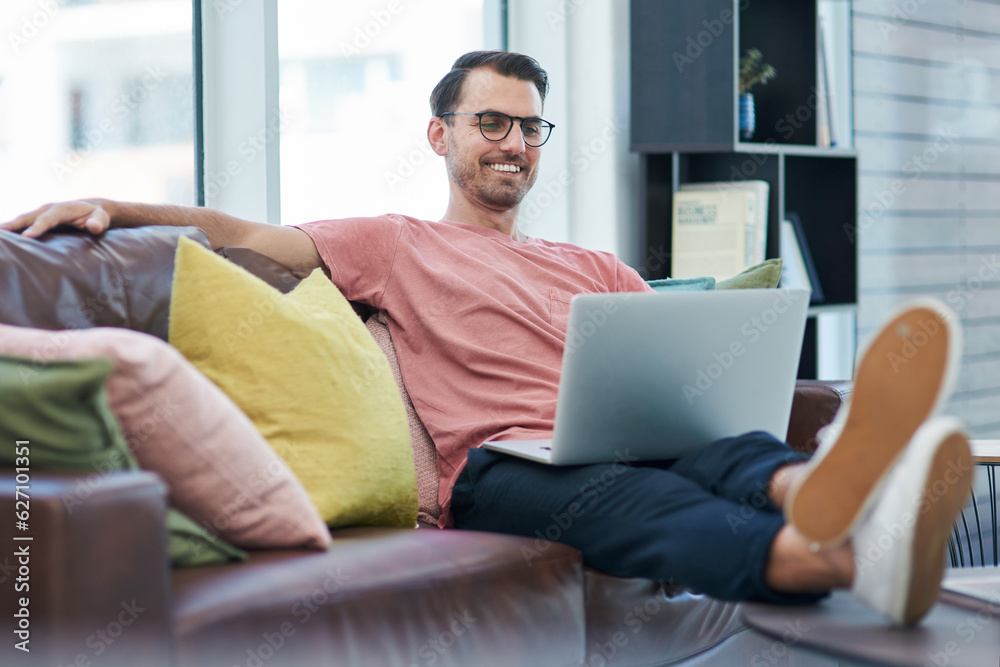 Poster High website traffic makes a happy entrepreneur. Shot of a young man using a laptop while relaxing on a sofa.