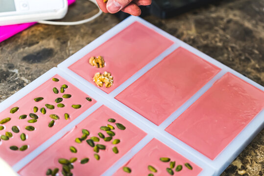 Decorating chocolate bars with nuts. Walnuts and pistachios places on ruby chocolate bars. Indoors closeup shot of chocolate producing process. Cooking appliances in background. High quality photo