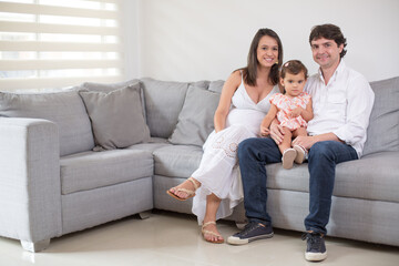 Smiling happy family portrait with the father carrying their little daughter on his lap and pregnant mother