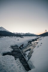 frozen river view from a wooden bridge on a snowy cold mountains at sunset with beautiful clear sky and white colors with a panoramic view