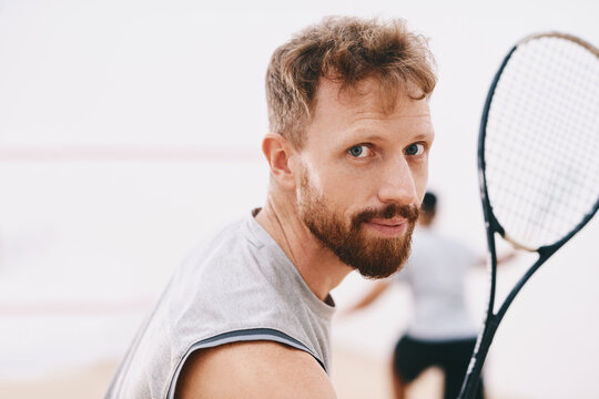 Have my medal ready for me. Portrait of a young man playing a game of squash with his team mate in the background.