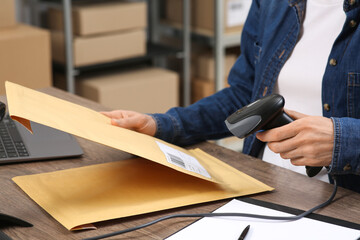 Seller with scanner reading parcel barcode in office, closeup. Online store
