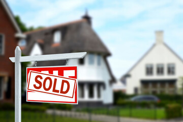 Red sale sign with Sold sticker near house