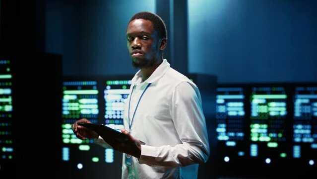 African american supervisor in server farm using tablet to find firewall misconfigurations affecting rackmounts performance and connectivity, leading to slow data transfer rates