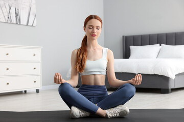 Young woman in sportswear meditating in bedroom