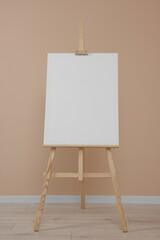 Wooden easel with blank canvas near beige wall indoors