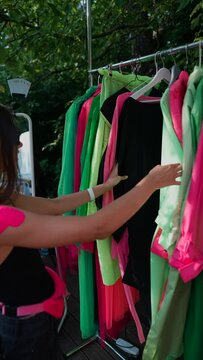 At the summer park fair, a young girl is choosing colorful clothing at a booth