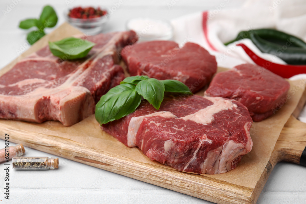 Wall mural cut fresh beef meat and basil leaves on white table, closeup