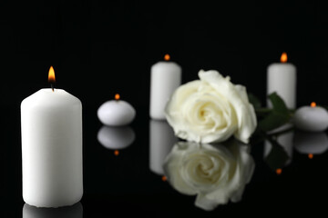 Fototapeta na wymiar White rose and burning candles on black mirror surface in darkness, closeup with space for text. Funeral symbols