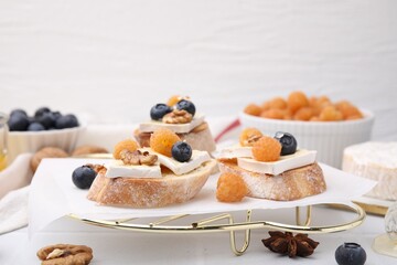 Tasty sandwiches with brie cheese, fresh berries and walnuts on white table. Space for text