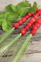 Grass stems with wild strawberries and leaves on wooden table, closeup