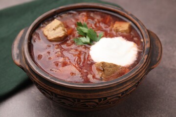 Tasty borscht with sour cream in bowl on brown textured table, closeup