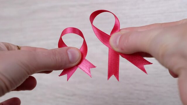 Female Hands Show Two Pink Ribbons on a Wooden White Background. Close up. Hand with a breast cancer symbol. Cancer information. Hope. October month. International AIDS, Cancer Day. Disease awareness.