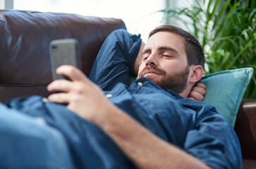 Recharge and bounce back better than ever. Shot of a young man using a smartphone while relaxing on...