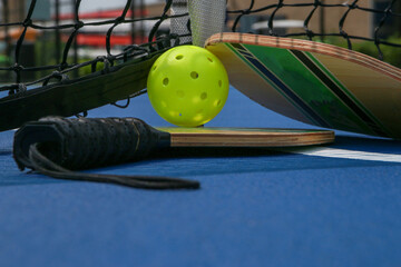 Close up of pickleball paddles and whiffle balls under a net on a court