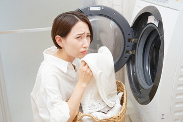洗濯機の前で洗濯物の匂いに悩むミドルエイジの女性