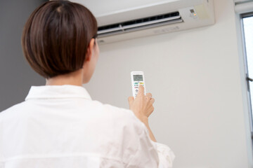 自宅のエアコンのリモコンを使う女性
