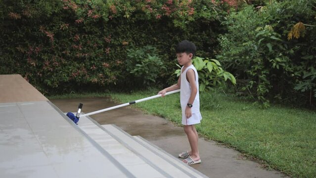 Asian boy is doing house chores by cleaning and wiping the floor of the balcony tiles with a water wiper mop.