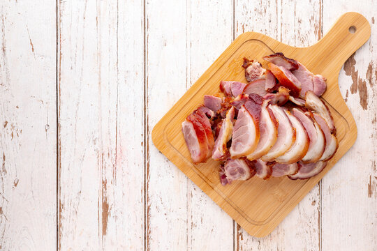 roasted pork knuckle eisbein slice in wooden cutting board on white wood texture background with copy space for text, top table view, flat lay, German food, pork leg
